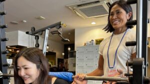 女性のお客様のスクワットを笑顔でサポートする原田理香トレーナー